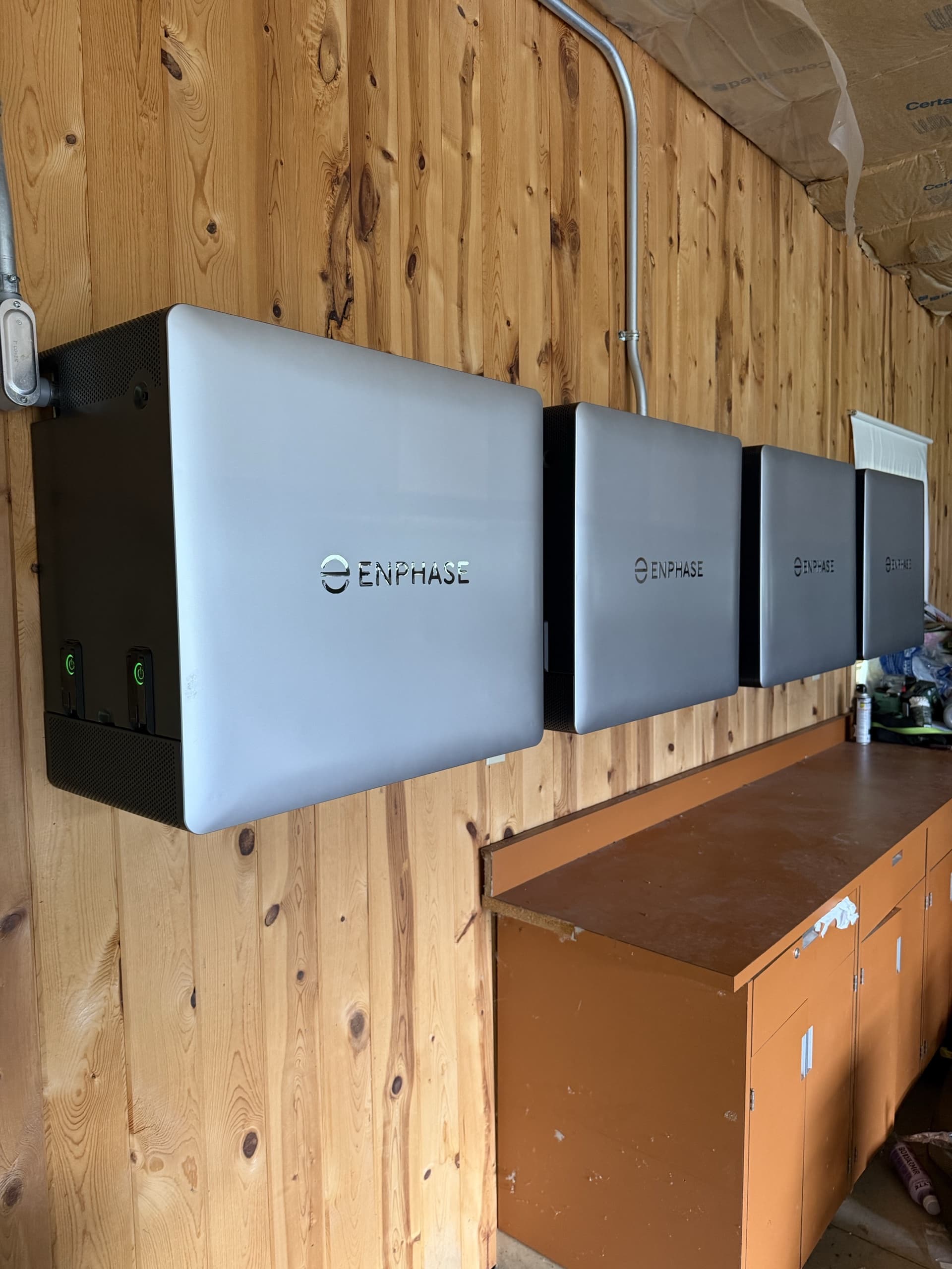 Four Enphase IQ Battery 10C units mounted in a row on a knotty pine wall