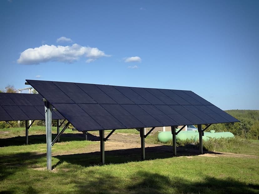 Two elevated off-grid ground array rows above a Wisconsin hillside, with propane tanks behind