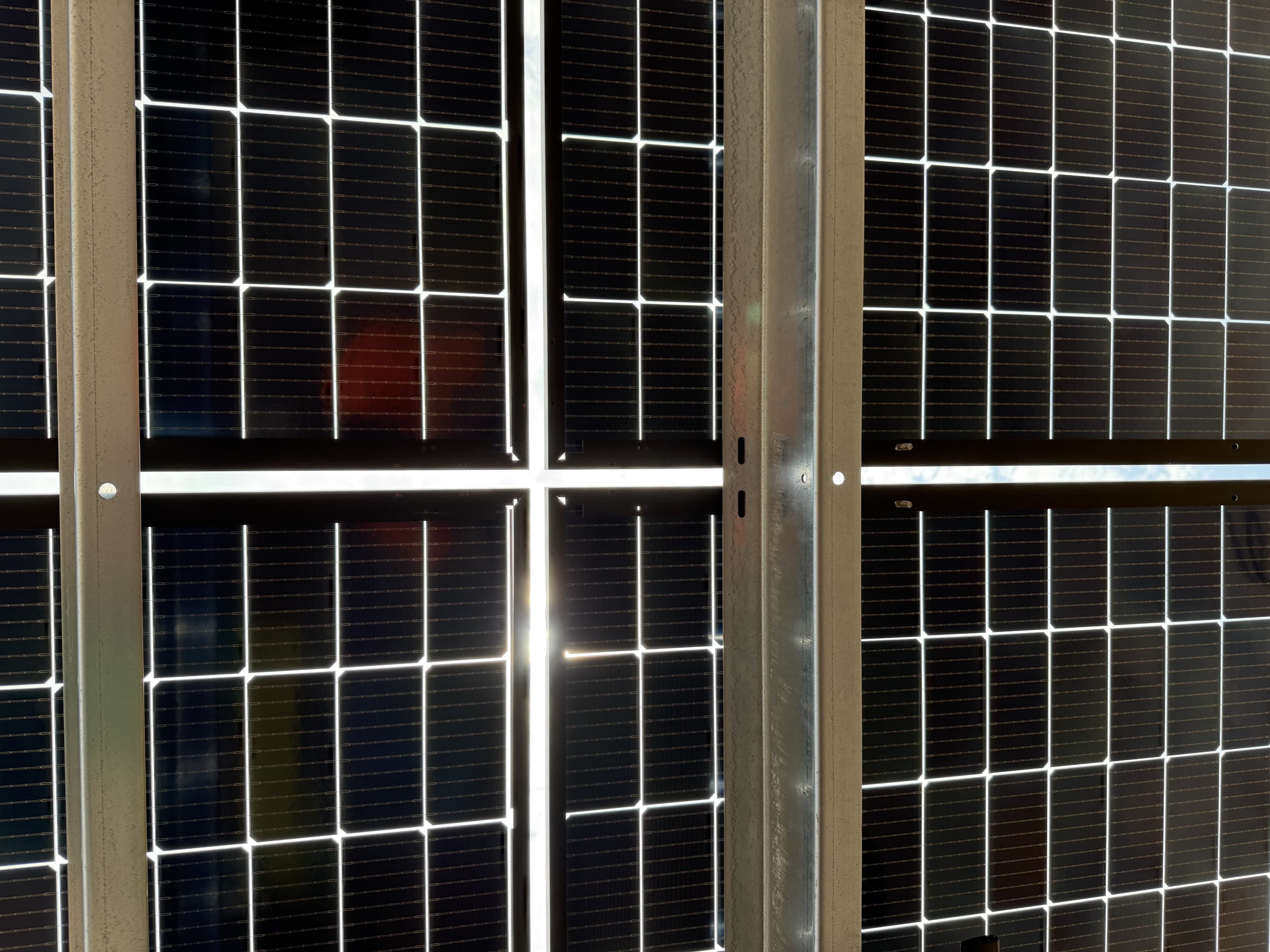 Sunlight forming a cross of light between all-black bifacial solar panels at Christ the Rock in Menasha, Wisconsin, photographed from beneath the array